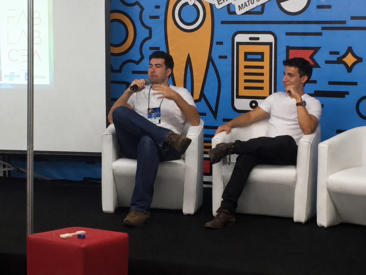 João speaking on a panel with a microphone beside another speaker
